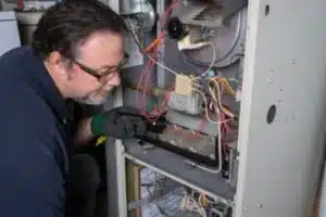 HVAC technician using flashlight to inspect interior components of gas furnace during preventative maintenance appointment
