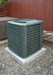 Outdoor central air conditioning unit installed on a concrete pad in a backyard, ready for spring
