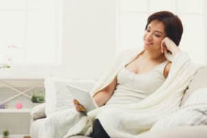 Woman relaxing comfortably on a sofa with a tablet, enjoying even home heating from a heat pump