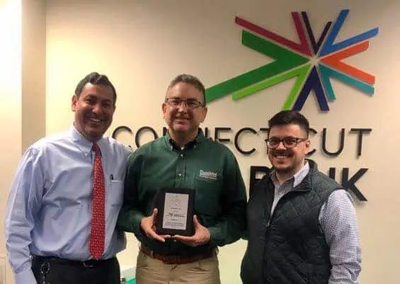 Jonathan Duncklee President of Duncklee Cooling and Heating holding Top Performer award plaque with two Connecticut Green Bank representatives at CT Green Bank headquarters Rocky Hill Connecticut