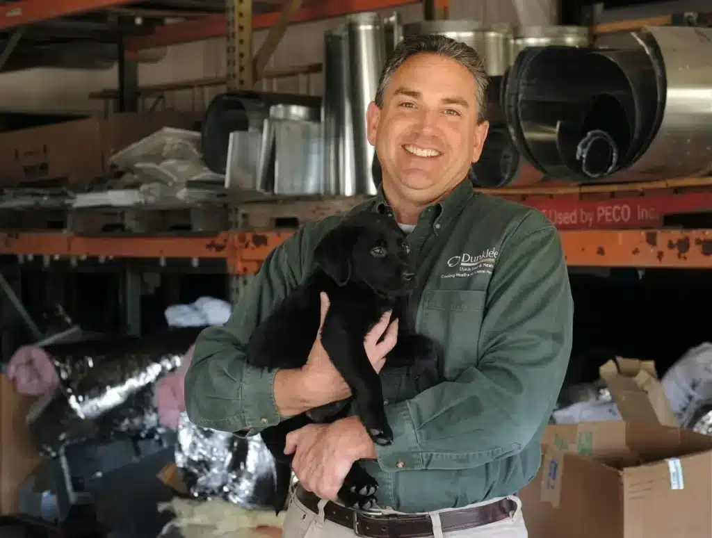 Jonathan Duncklee vice president of Duncklee Cooling and Heating holding his 8-week-old black puppy Jessie at company facility in Stonington Connecticut
