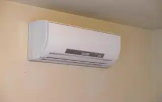 White wall-mounted ductless mini-split air handler unit installed high on beige wall for efficient home heating and cooling