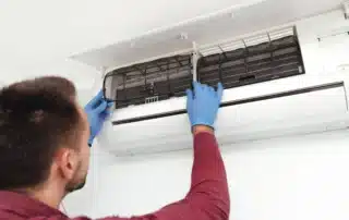 HVAC technician in maroon shirt wearing blue gloves removing and cleaning dirty filter from wall-mounted mini-split air handler to prevent AC short-cycling