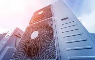 Low angle view looking up at large commercial HVAC rooftop condenser units against blue sky representing common commercial building heating and cooling systems
