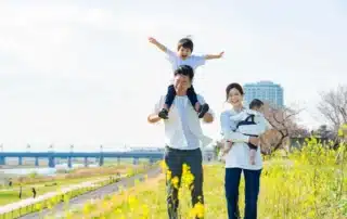 Happy family with father carrying child on shoulders and mother holding baby walking through yellow wildflower field on mild spring day in Connecticut