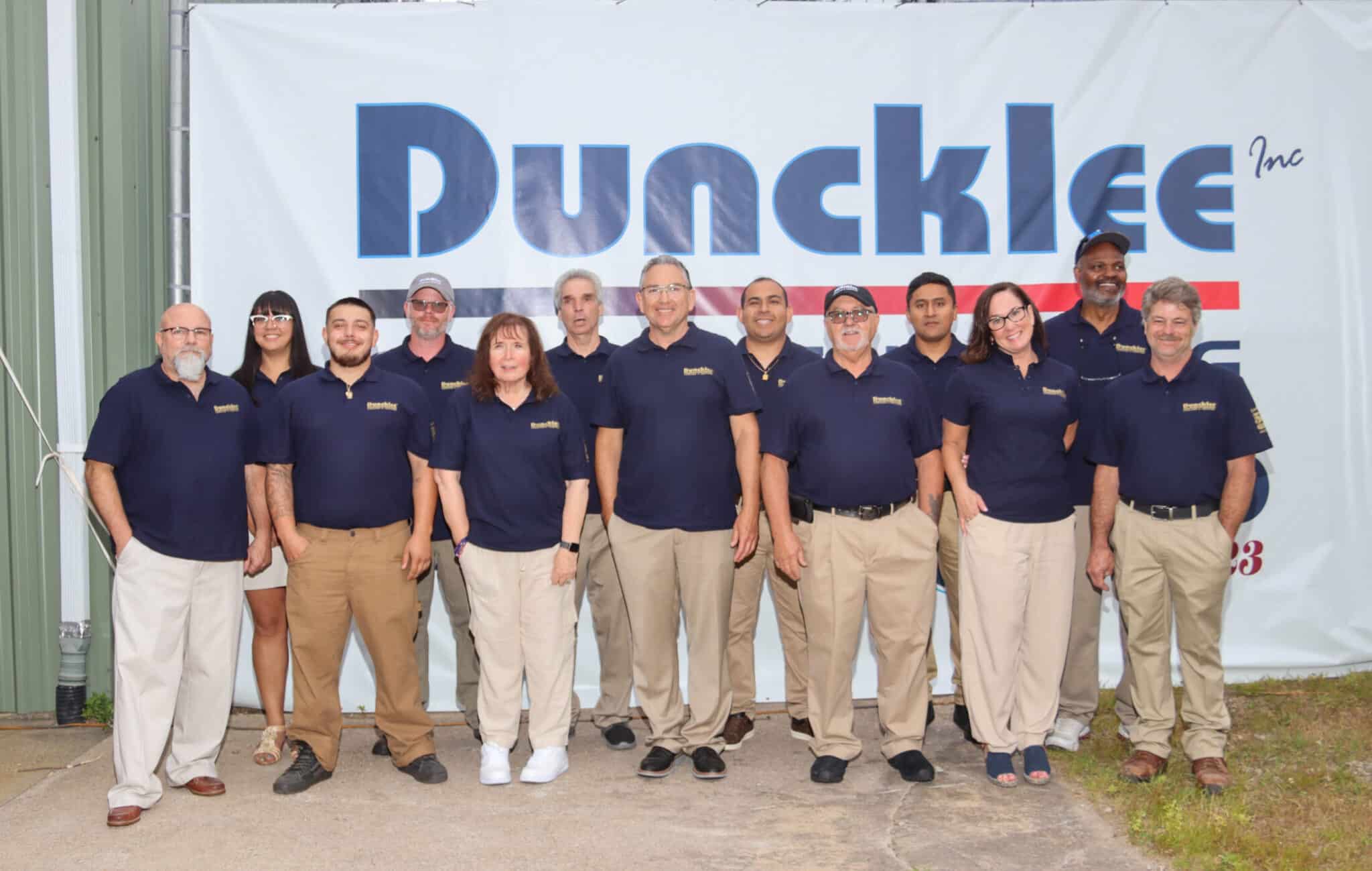 Duncklee Cooling and Heating Leadership Team Mystic The leadership team of Duncklee Cooling and Heating posing in front of an anniversary banner in Mystic, CT